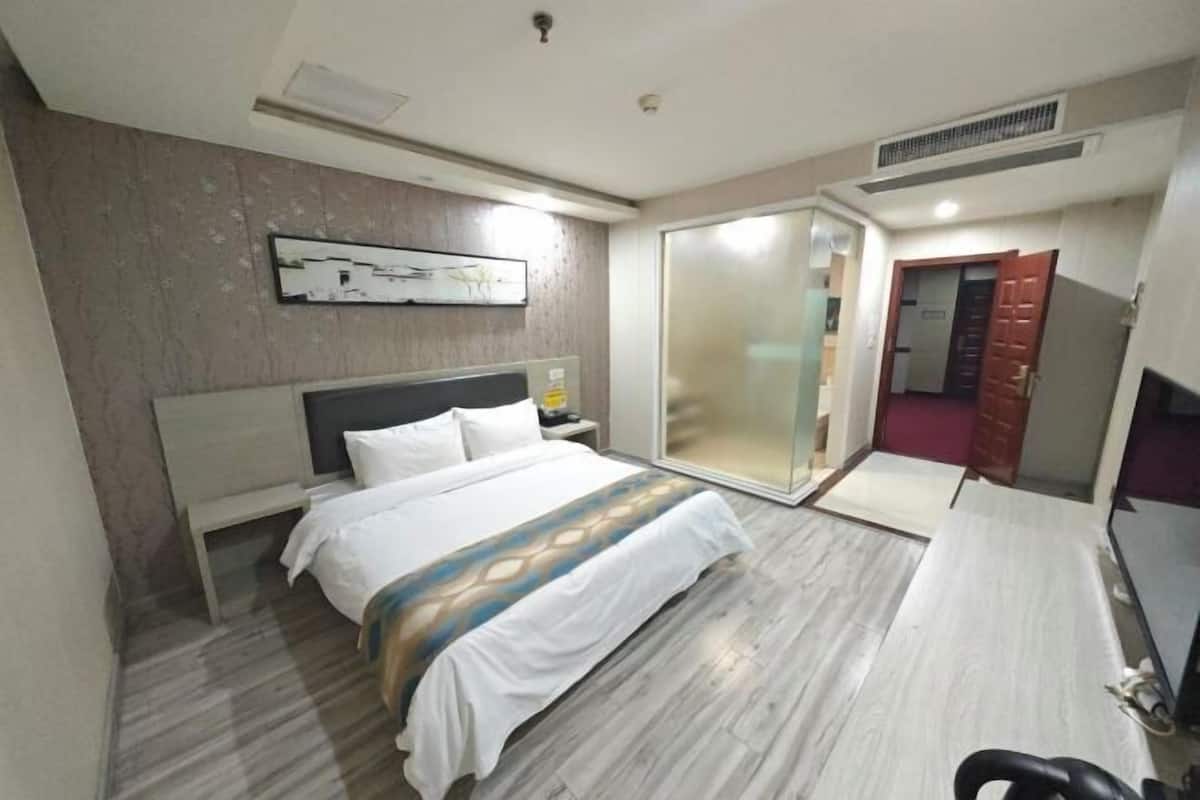 A hotel room with a bed, a desk, a chair, a wardrobe, and a sliding door to a bathroom.