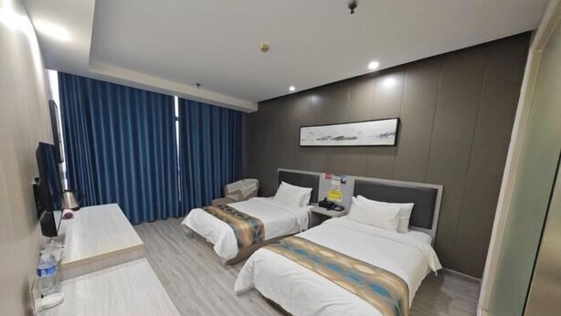 Habitación de hotel con dos camas, un escritorio, un televisor de pantalla plana y un ventanal grande con cortinas azules.