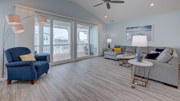 A spacious living room with a blue armchair, a grey sofa, a round coffee table, and a ceiling fan.