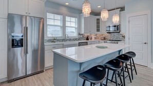 A modern kitchen with stainless steel appliances, a central island with bar stools, and pendant lighting.