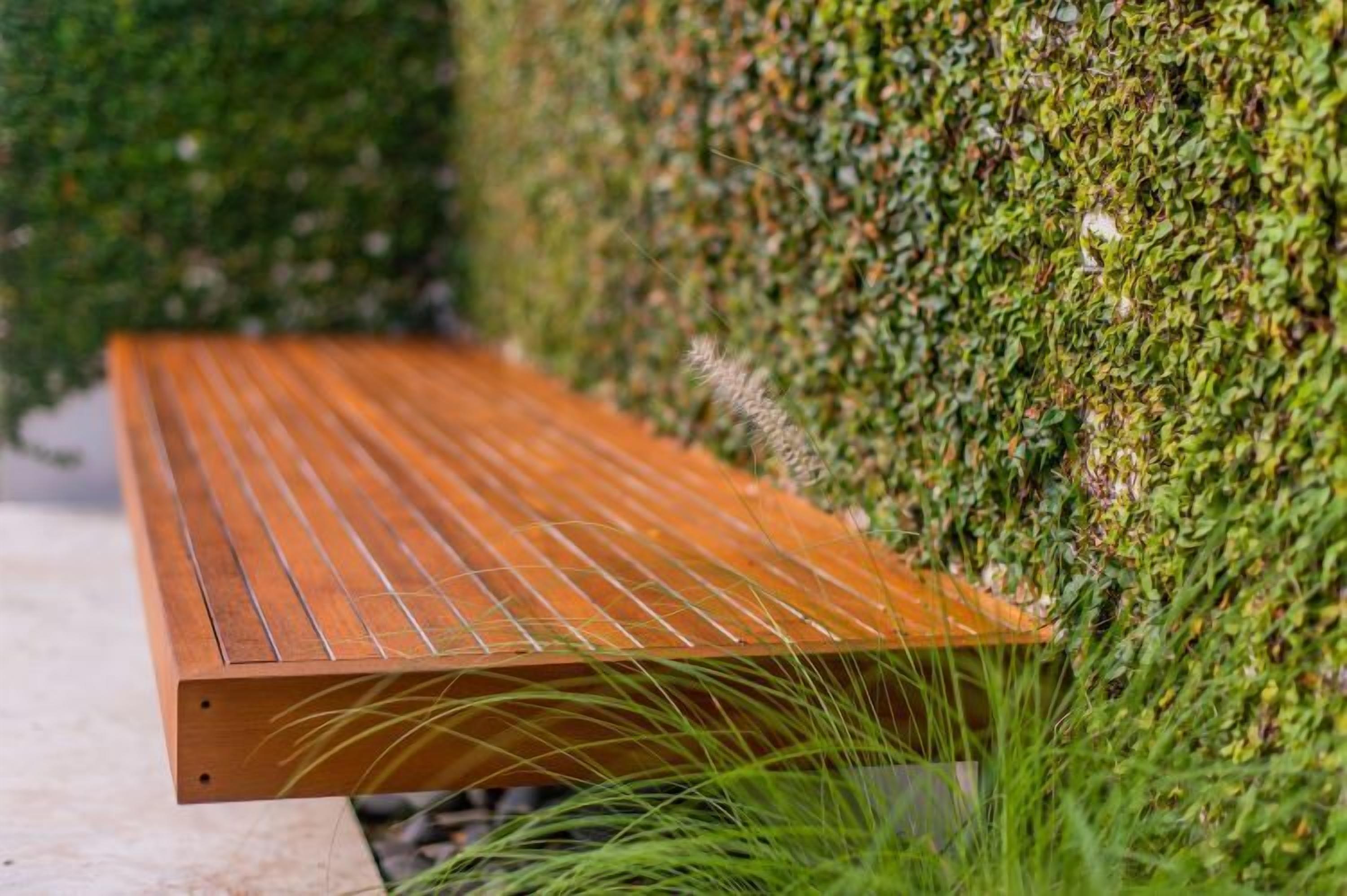 A wooden bench with slatted design, positioned against a wall covered in dense green foliage.