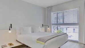 Un dormitorio moderno con una cama grande, una mesita de noche, una ventana con persianas y vistas al exterior.