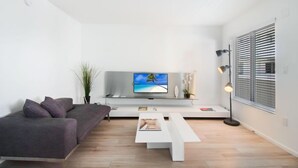 Una sala de estar moderna con un sofá, una mesa de centro, un televisor y una lámpara de pie.