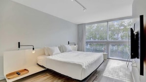 A modern bedroom with a bed, bedside tables, a TV, and a window with blinds.