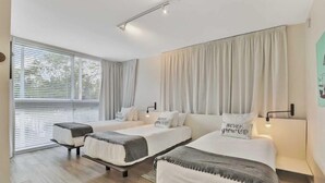Quarto de hotel moderno com duas camas de solteiro, uma janela grande com persianas e vista para o exterior.