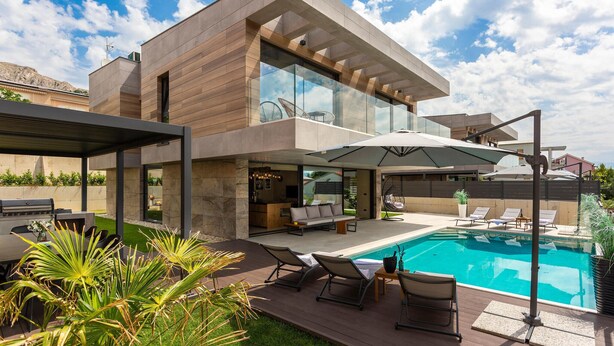 Ein modernes Haus mit Swimmingpool, Außenmöbeln und einer Pergola.