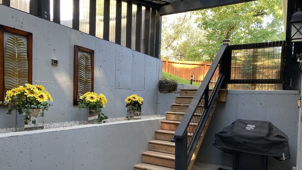 Een trap die leidt naar een terras met een barbecue en bloemen op de muur.