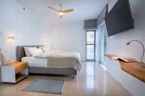 Una camera da letto moderna con un letto, comodini, una ventola a soffitto, un televisore montato a parete e una finestra con persiane.