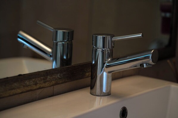 A bathroom with a chrome faucet and a mirror reflecting the sink and faucet.