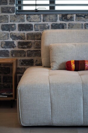A sofa with a textured fabric, a cushion with a patterned cover, and a wooden side table with a book. - Stylish 2BR Tel Aviv • Luxury & Ease by SeaNRent (Tel Aviv-Yafo)