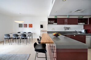 Una cucina moderna con isola centrale, zona pranzo con sedie e lavandino a vista.