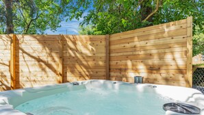 Un jacuzzi en un entorno exterior de madera, con un cerco de madera y árboles al fondo.