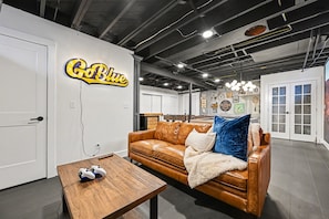 A modern living room with a leather couch, a wooden coffee table, and a neon sign that reads "Go Blue".