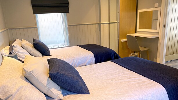Une chambre d’hôtel avec deux lits, une fenêtre avec des stores, un miroir et un bureau avec une chaise.