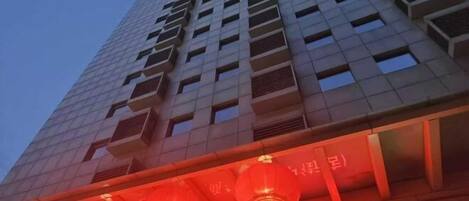 A tall building with a commercial space on the ground floor, featuring a row of red lanterns and a sign in Chinese characters.