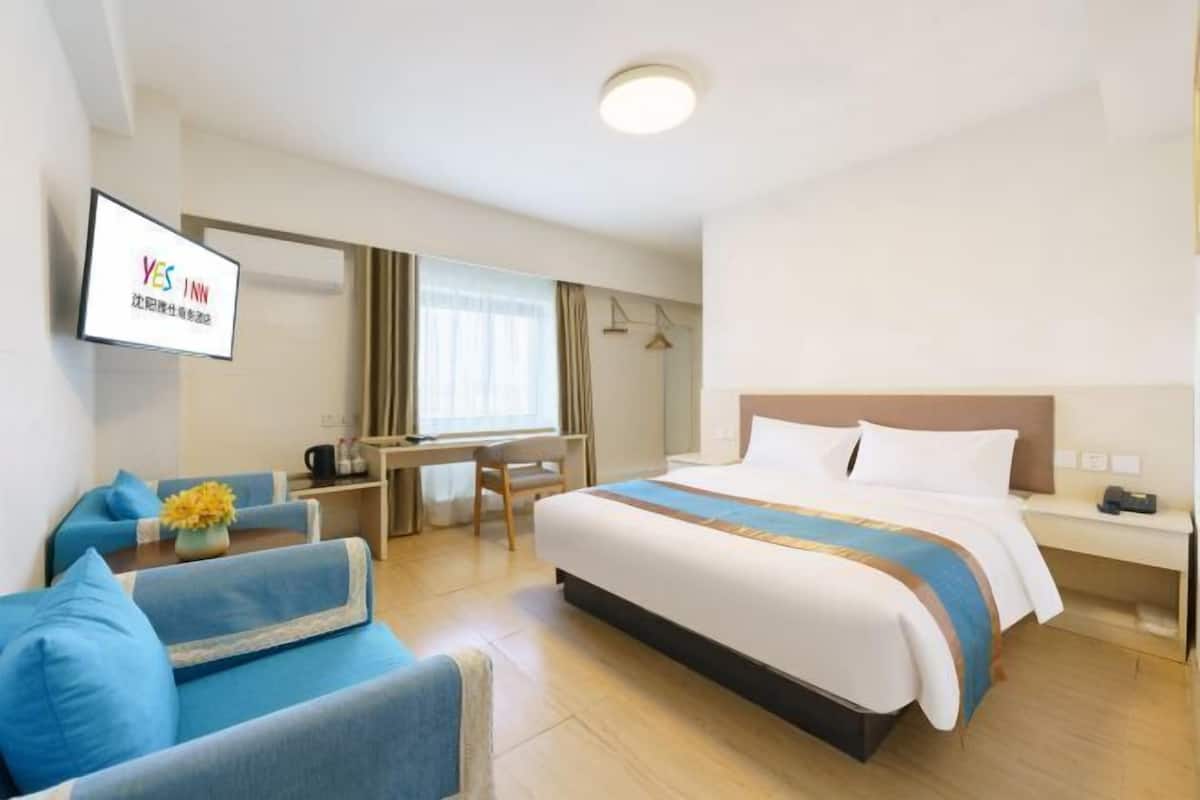 Hotellihuone, jossa on sänky, työpöytä, tuoli ja seinälle asennettu televisio.