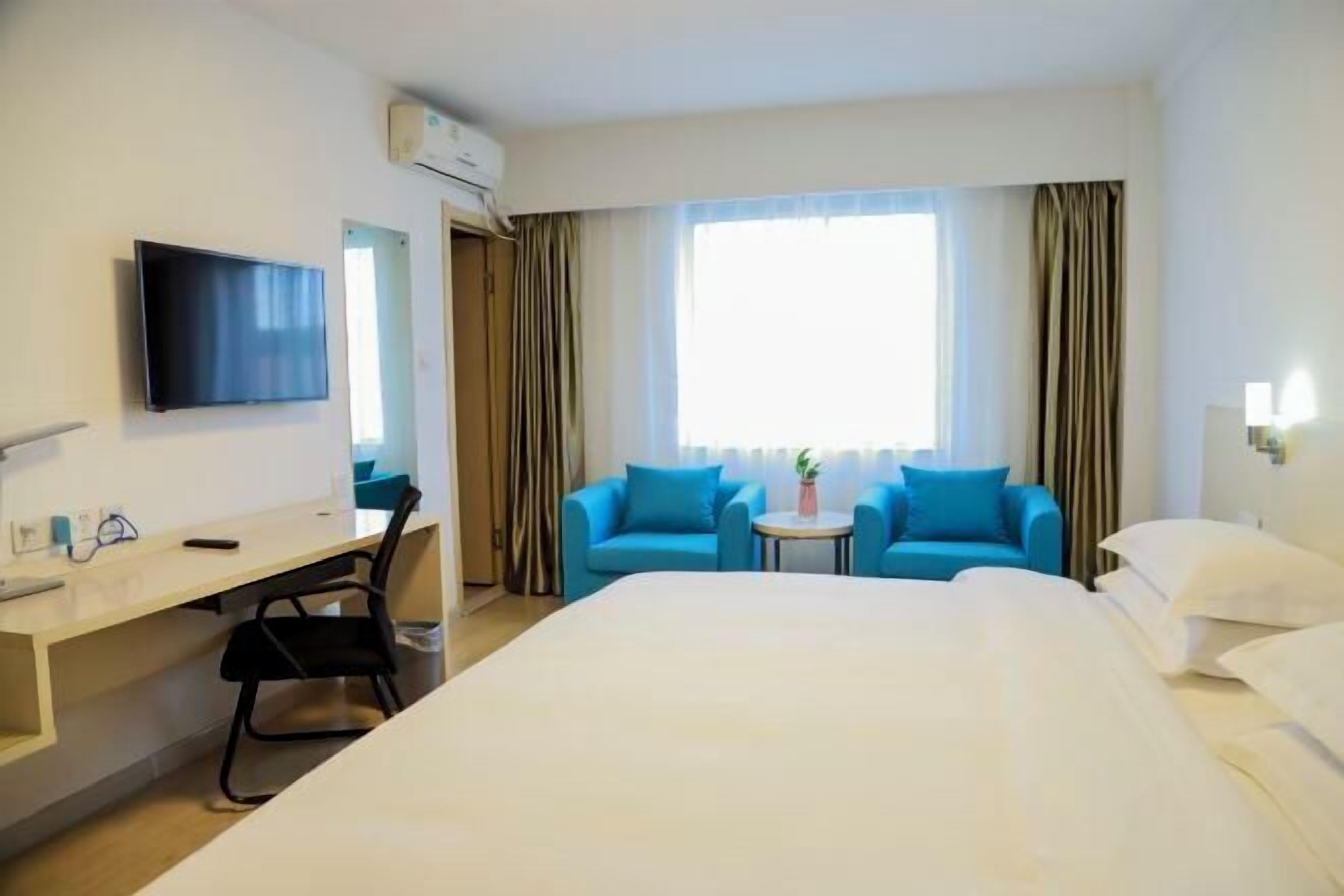 Habitación de hotel con cama, escritorio, silla, televisor y ventana con cortinas.