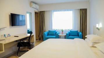 Habitación de hotel con cama, escritorio, silla, televisor y ventana con cortinas.