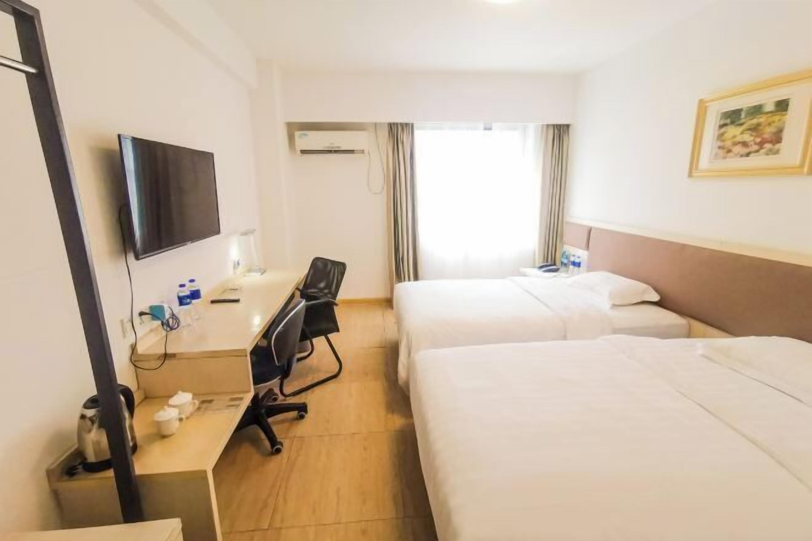 A hotel room with a bed, a desk with a chair, a television, and a window with curtains.