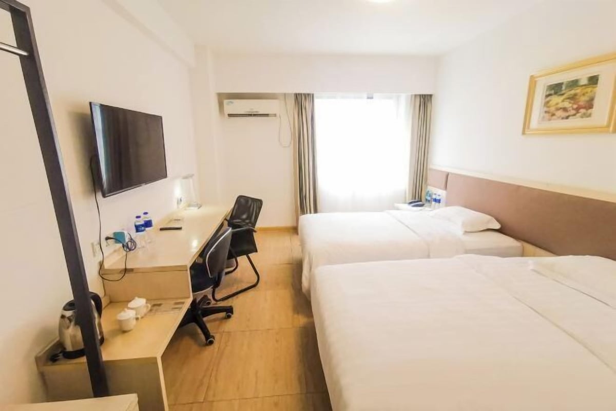 A hotel room with a bed, a desk with a chair, a television, and a window with curtains.