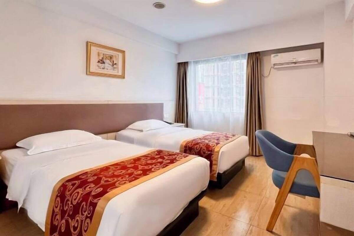 Hotellihuone, jossa on kaksi sänkyä, työpöytä, tuoli ja ilmastointilaite.