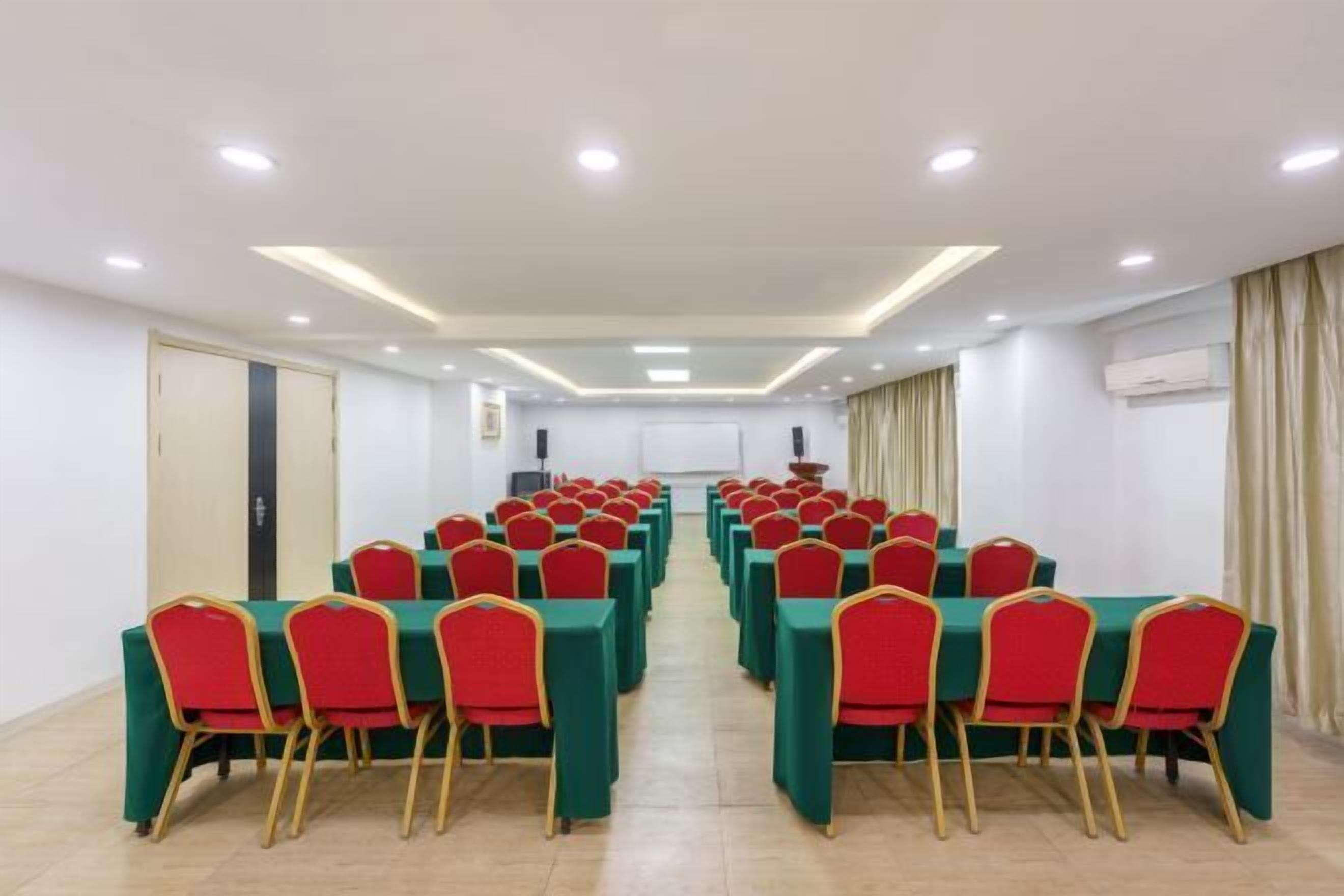 A conference room with rows of tables and chairs, equipped with ceiling lights and an air conditioning unit.
