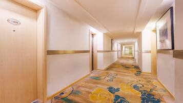 Un pasillo de hotel con puertas a la izquierda, una alfombra estampada y cuadros en las paredes.