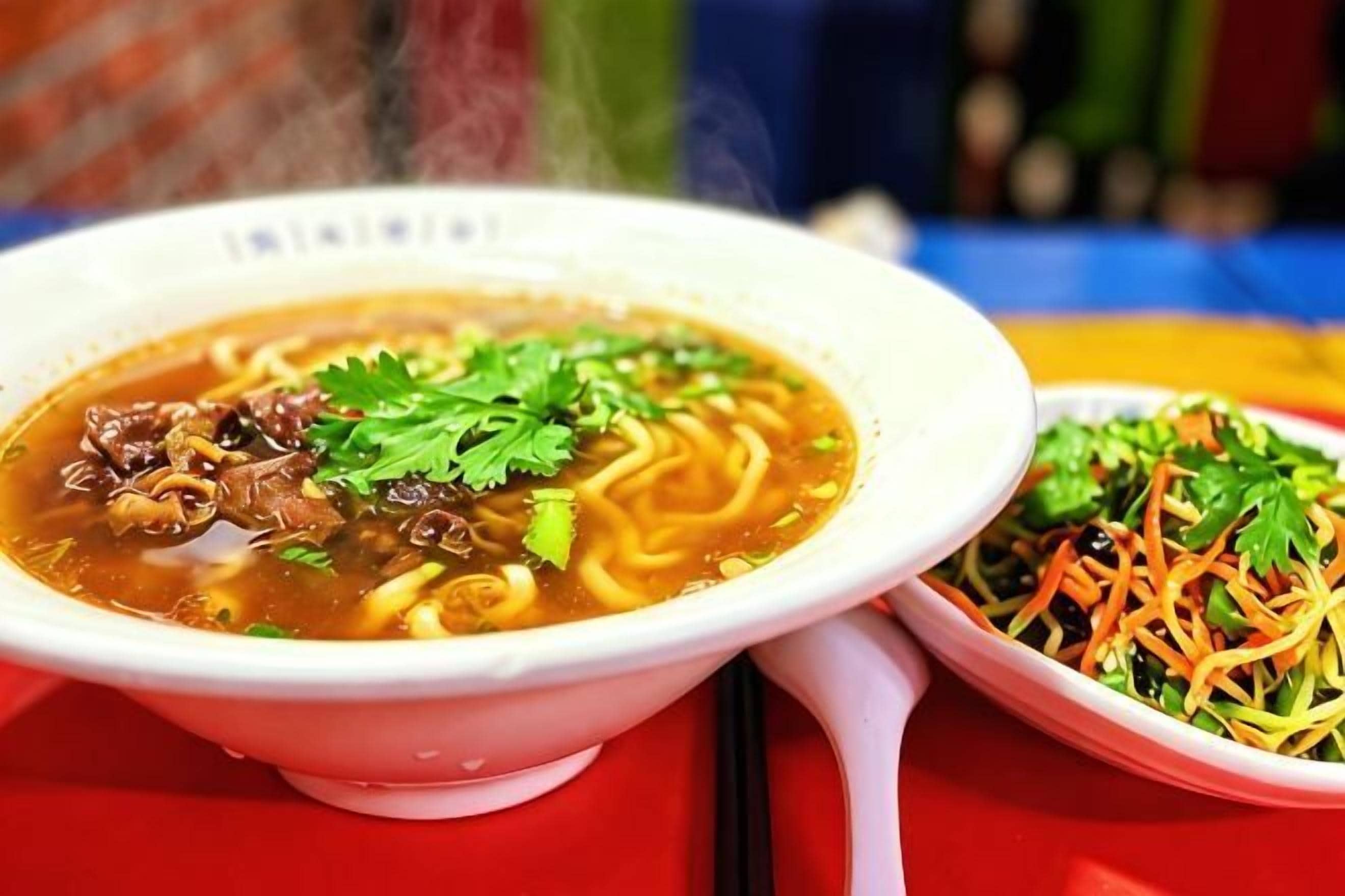 A bowl of soup with noodles and a side salad.