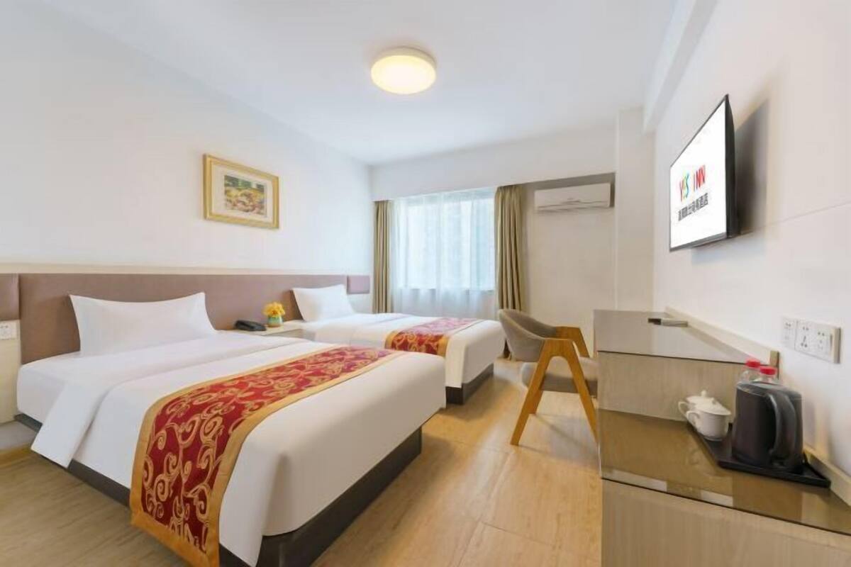 Hotellihuone, jossa on kaksi sänkyä, televisio, työpöytä, jossa on kahvinkeitin, ja ikkuna, jossa on verhot.