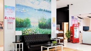 A modern lobby with a black sofa, a coffee table, a red vending machine, and a large painting of a landscape. - Longemont Yashi Business Hotel (Zhongjie Street，Shenyang) (Shenyang)
