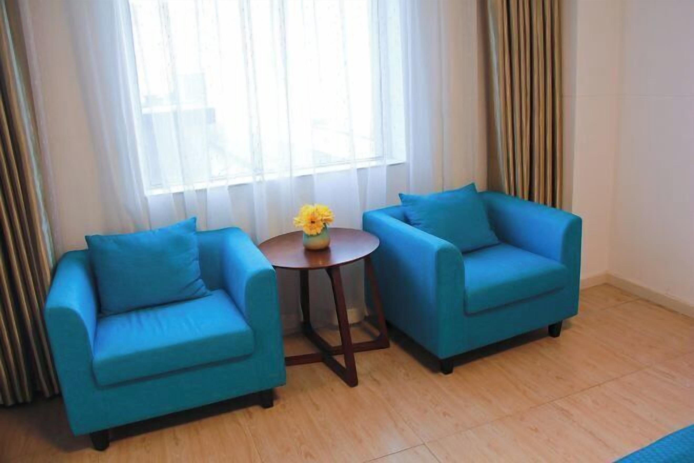 Een kamer met twee blauwe fauteuils en een kleine ronde tafel met een vaas gele bloemen.