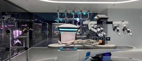 Egy jövőbeli, korszerű orvosi létesítmény, robotikai berendezésekkel, központi vezérlőállomással és kör alaprajzzal.