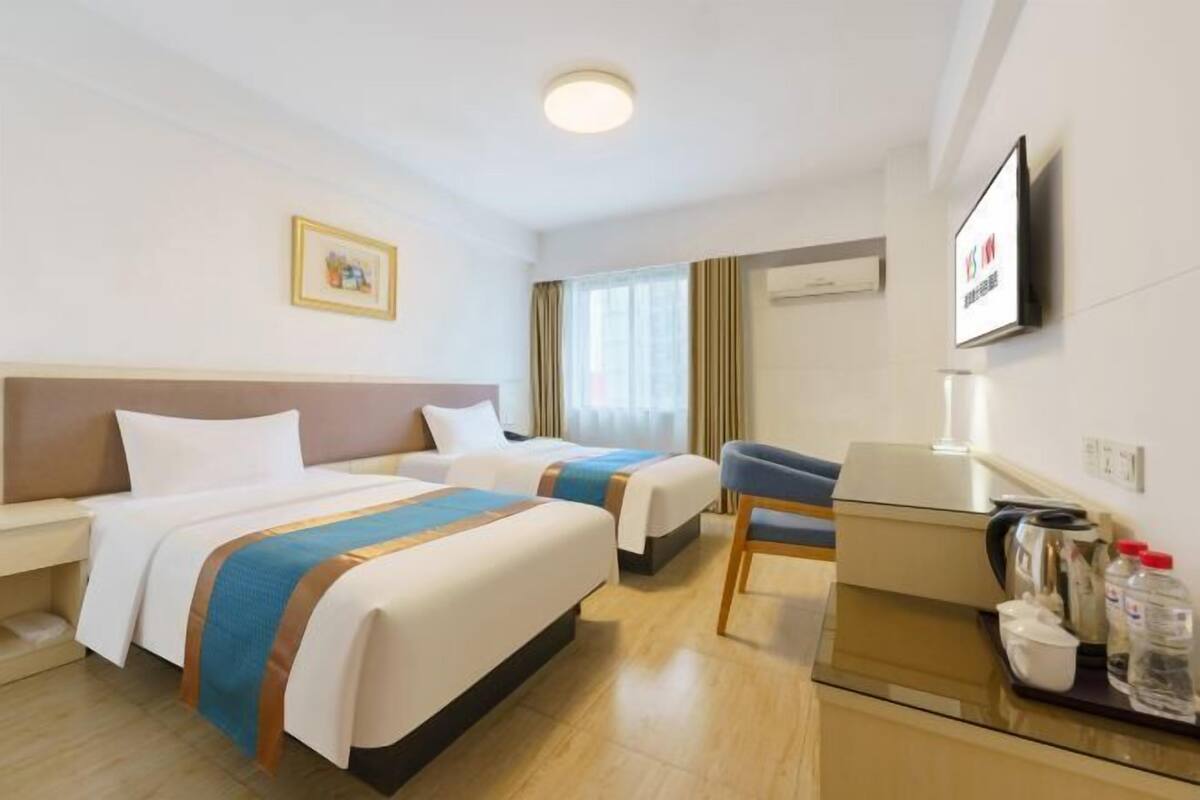 Hotellihuone, jossa on kaksi sänkyä, työpöytä, tuoli, televisio ja taulu seinällä.