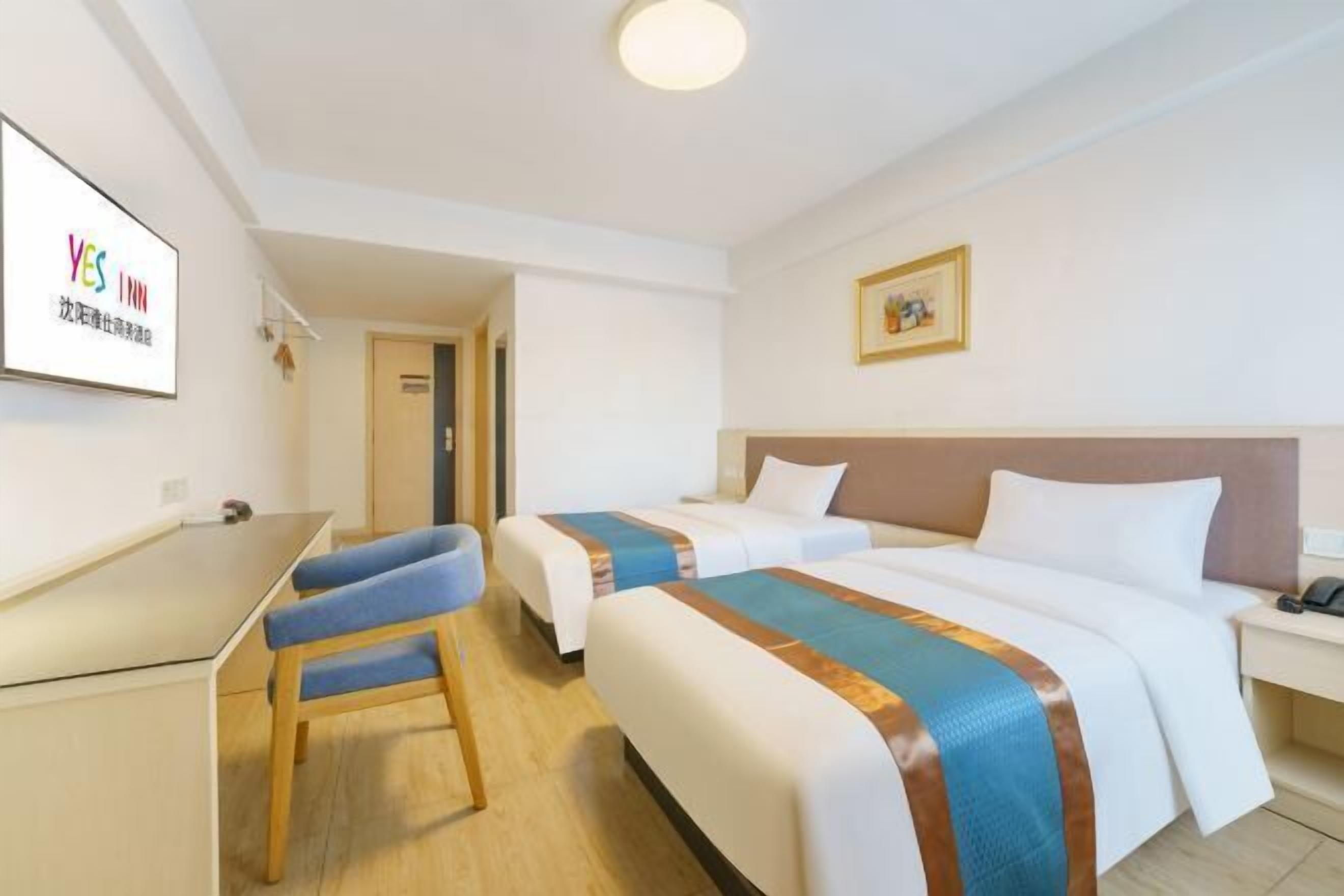 A hotel room with two beds, a desk, and a chair.