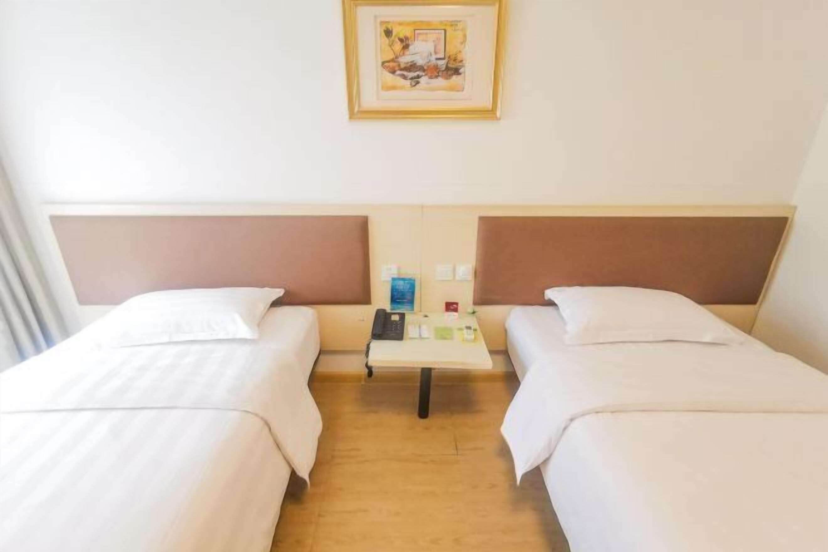 Een hotelkamer met twee enkele bedden, een klein tafeltje met toiletartikelen en een ingelijst schilderij aan de muur.