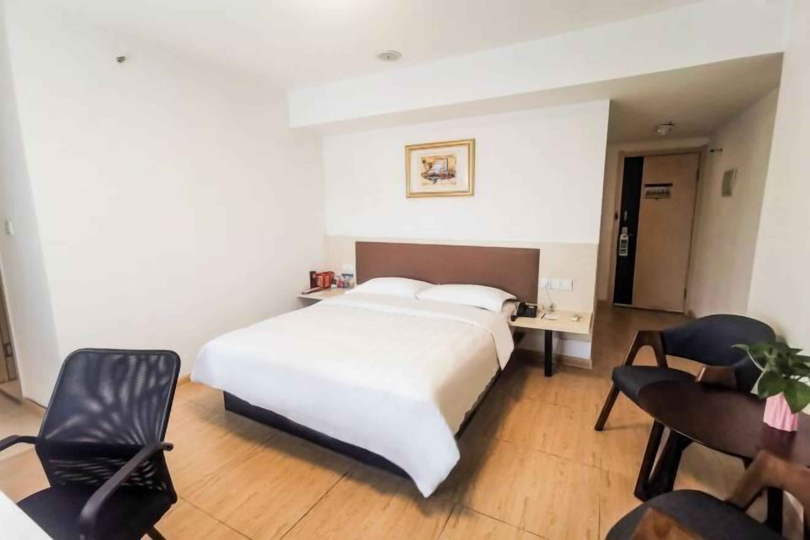 A hotel room with a bed, a nightstand, a chair, a desk, and a framed picture on the wall.