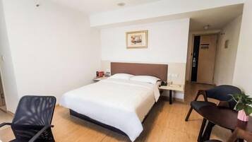 A hotel room with a bed, a nightstand, a chair, a desk, and a framed picture on the wall.