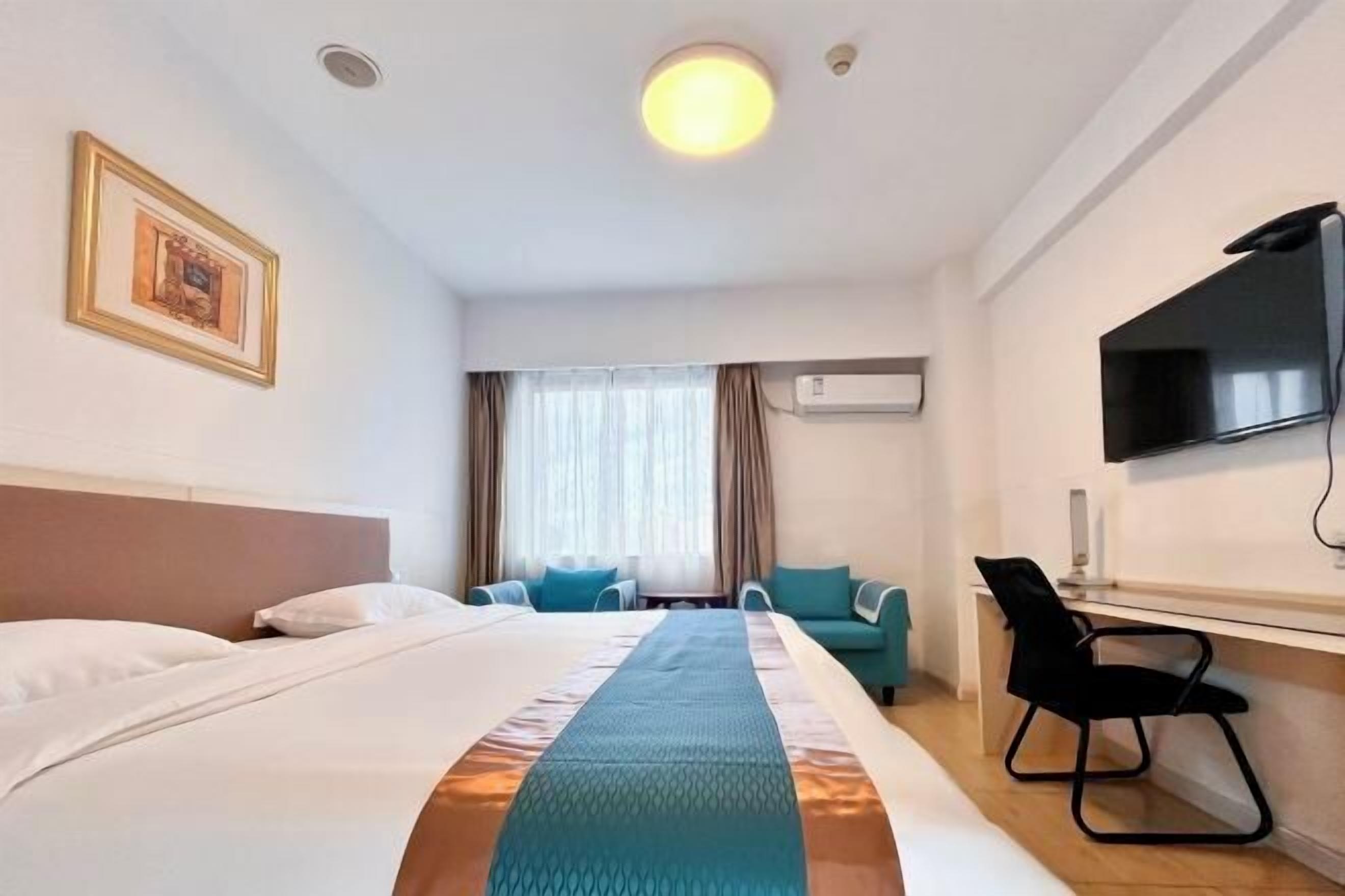 A hotel room with a bed, a desk, a chair, a television, and an air conditioning unit.
