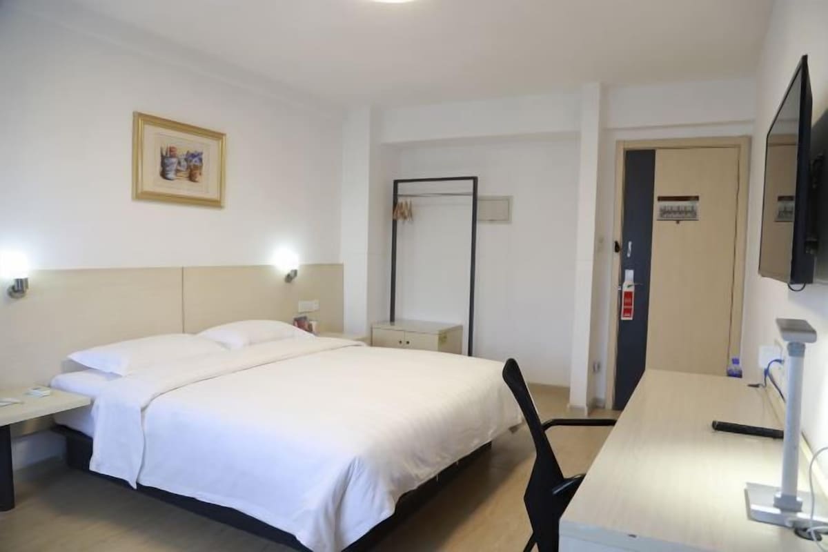 A hotel room with a bed, bedside table, lamp, chair, desk, and a television.