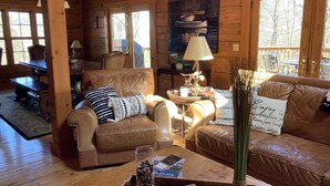 Een gezellig cabin interieur met houten details, leren banken, een eettafel en uitzicht op de natuur door grote ramen.