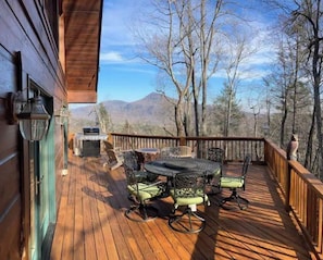 A wooden deck with outdoor furniture, a grill, and a view of mountains.
