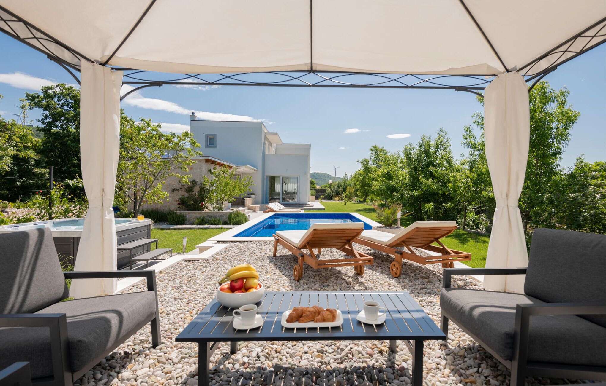 Un espacio al aire libre cubierto con piscina, sillas de descanso y una mesa con comida y bebidas.