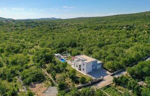 Una casa moderna de dos pisos con piscina, rodeada de abundante vegetación y colinas.