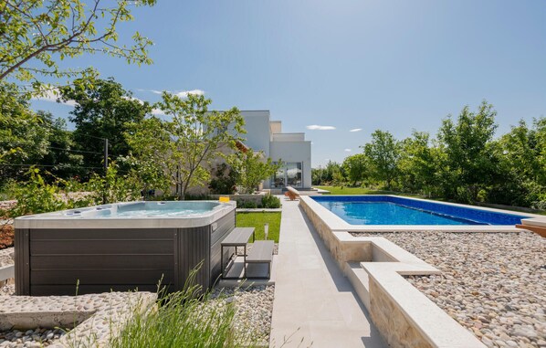 Un área de piscina moderna al aire libre con un jacuzzi, un patio con asientos y una vista de un edificio contemporáneo al fondo.