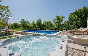 Relax by the serene pool and hot tub surrounded by lush greenery and trees.