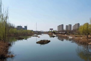 A calm river with a bridge, trees, and buildings in the background.