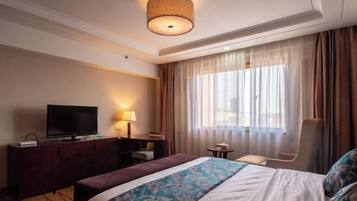 A hotel room with a bed, a television on a dresser, a desk with a chair, and a window with curtains.
