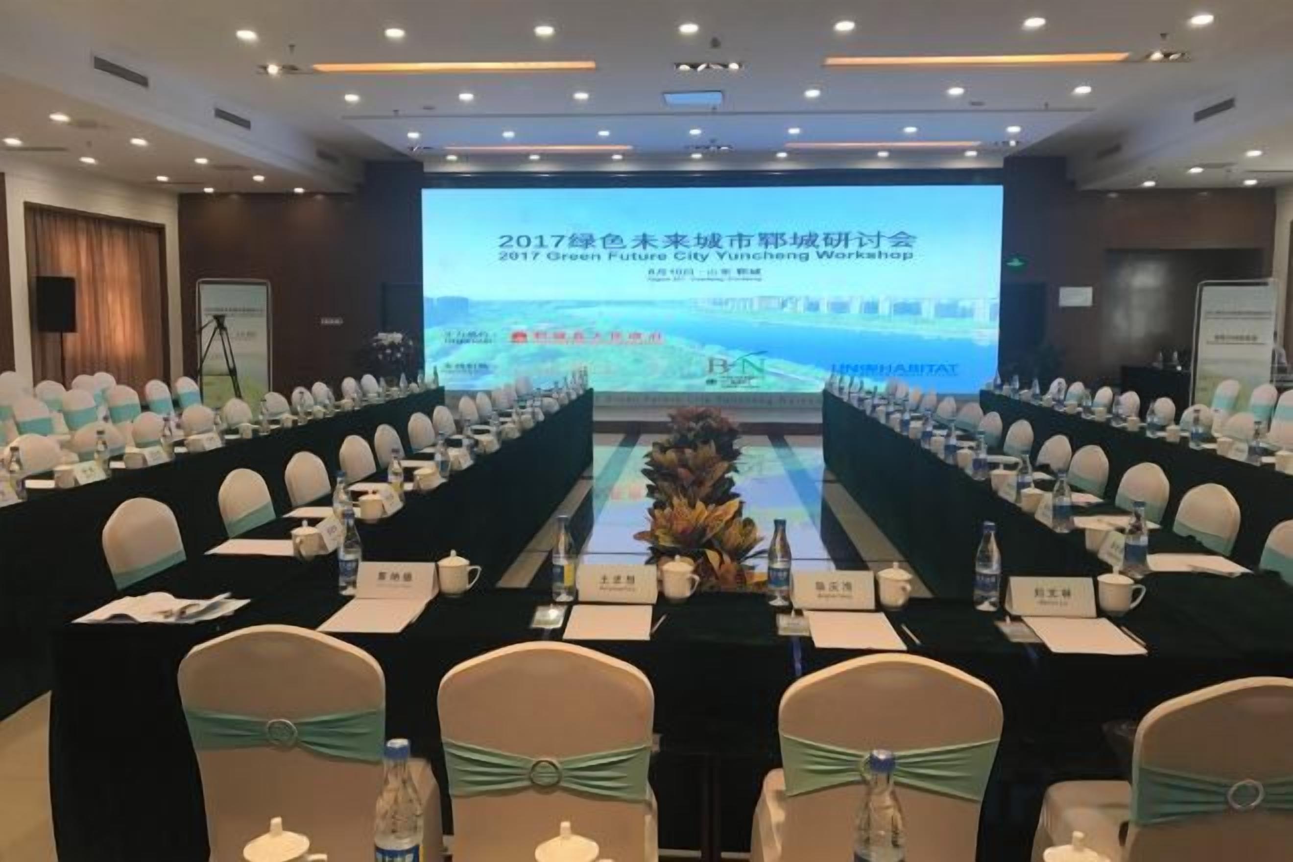 A conference room with a long table, chairs, and a presentation screen.