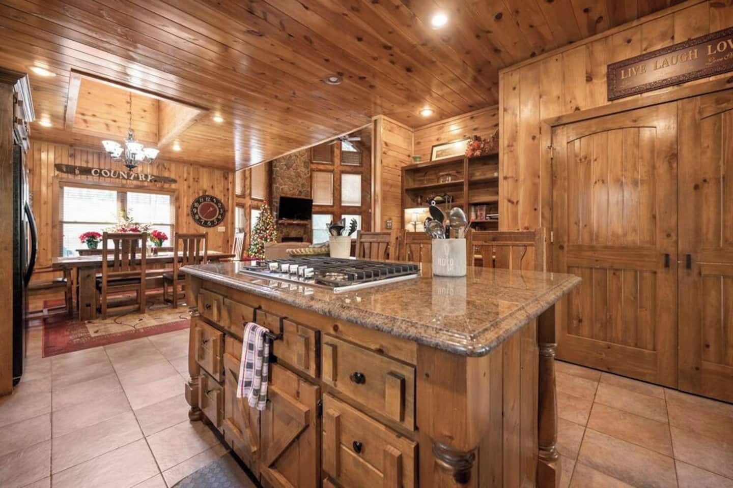 Un intérieur en bois avec un îlot de cuisine, des armoires en bois et un coin repas agrémenté d’un sapin de Noël.