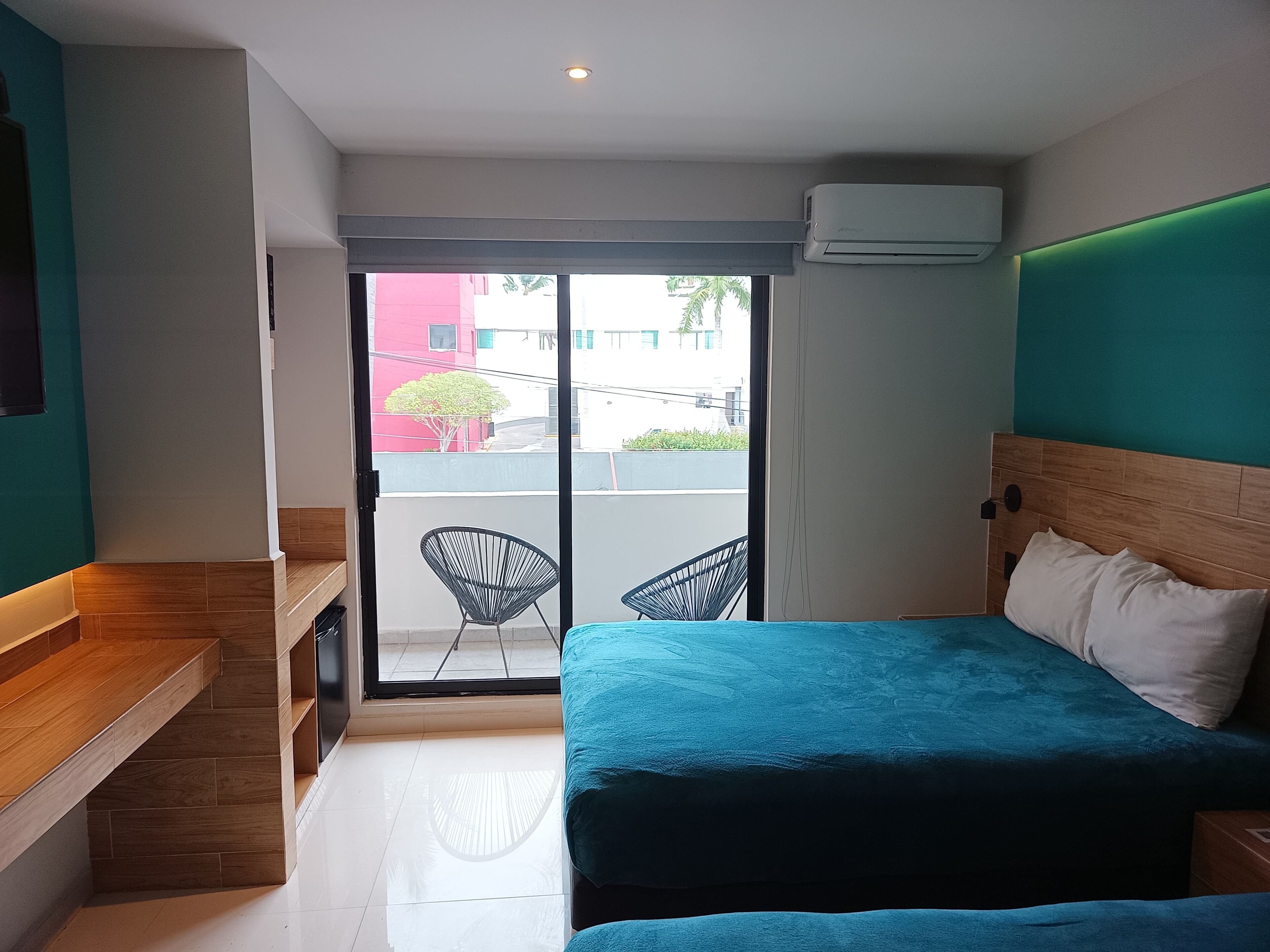 Habitación de hotel con cama, escritorio, silla y puerta corrediza de vidrio que da a un espacio exterior.